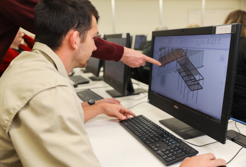 A ULM Construction Management student looks at construction measurements on a computer. A professor's hand points at the screen.