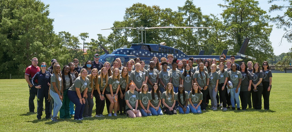 A group of about 50 young people wearing matching t-shirts stand in front of a helicopter.