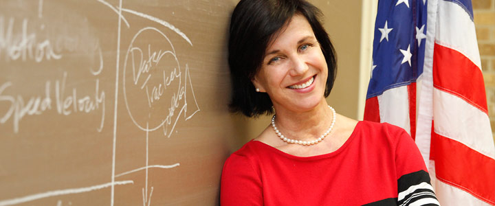 Lynn Clark smiling in classroom by chalkboard photo of professor or instructor