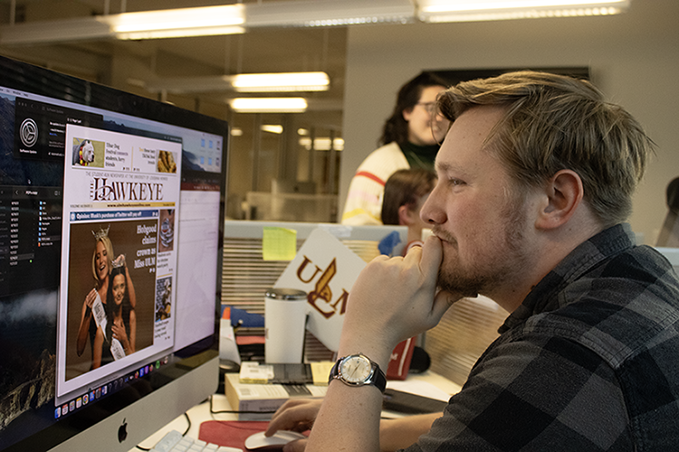 A man wearing a checked shirt looks at a computer screen of a Hawkeye newspaper design.