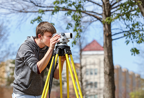 A ULM Construction Management student surveys outside on campus.