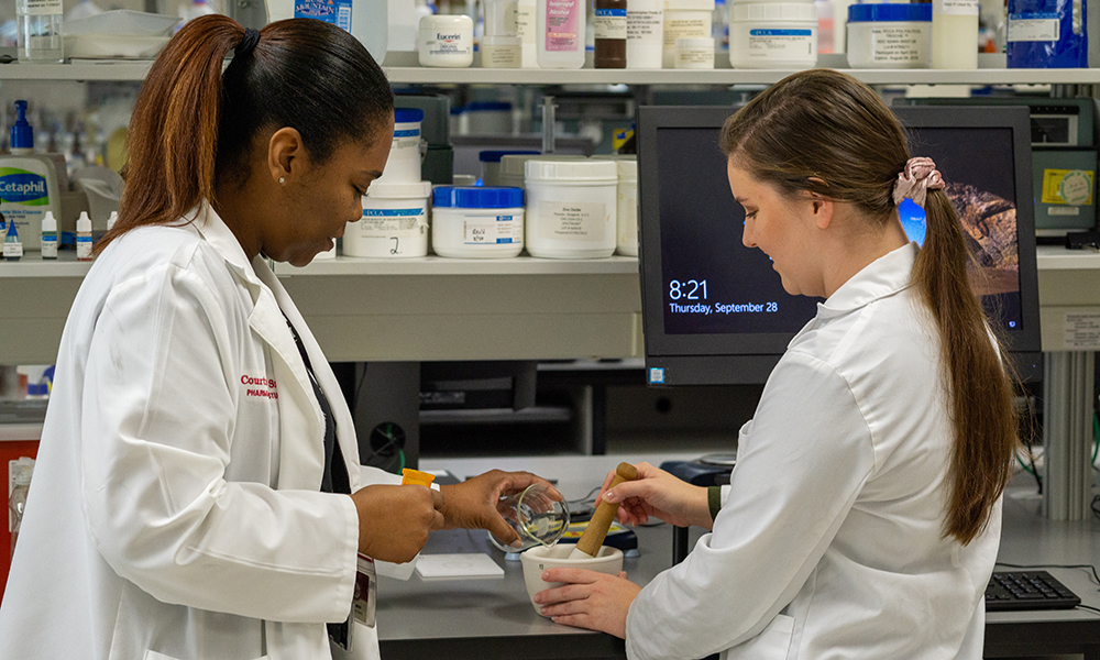 Two women wearing white coats work in a lab