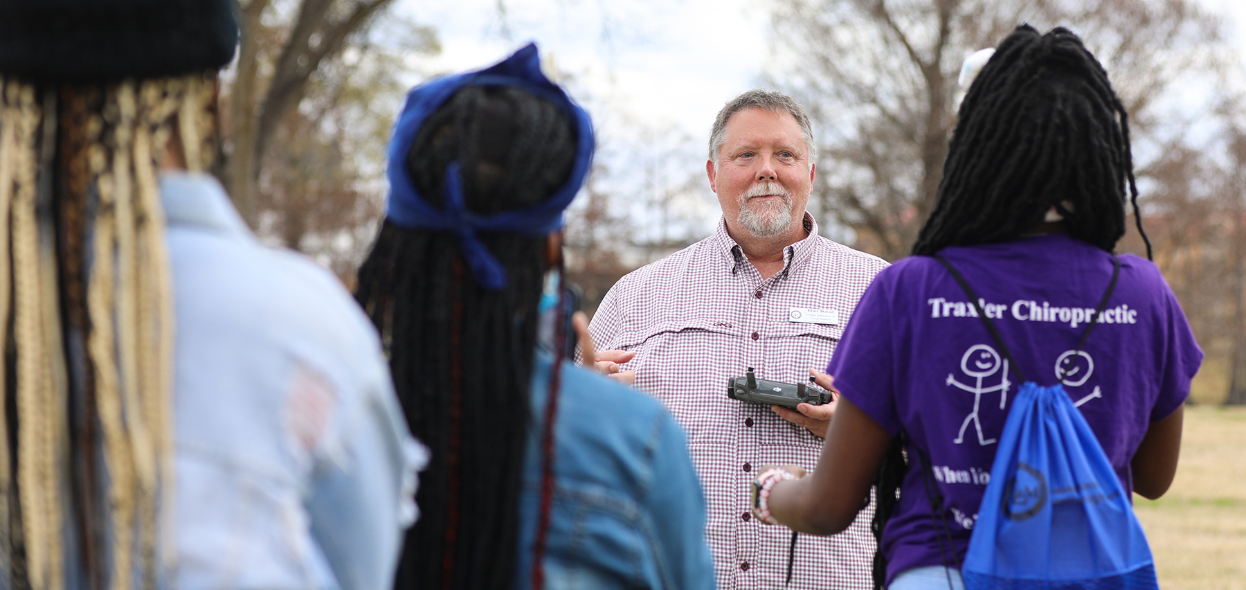 A ULM professor holds a drone and teaches three students outdoors.