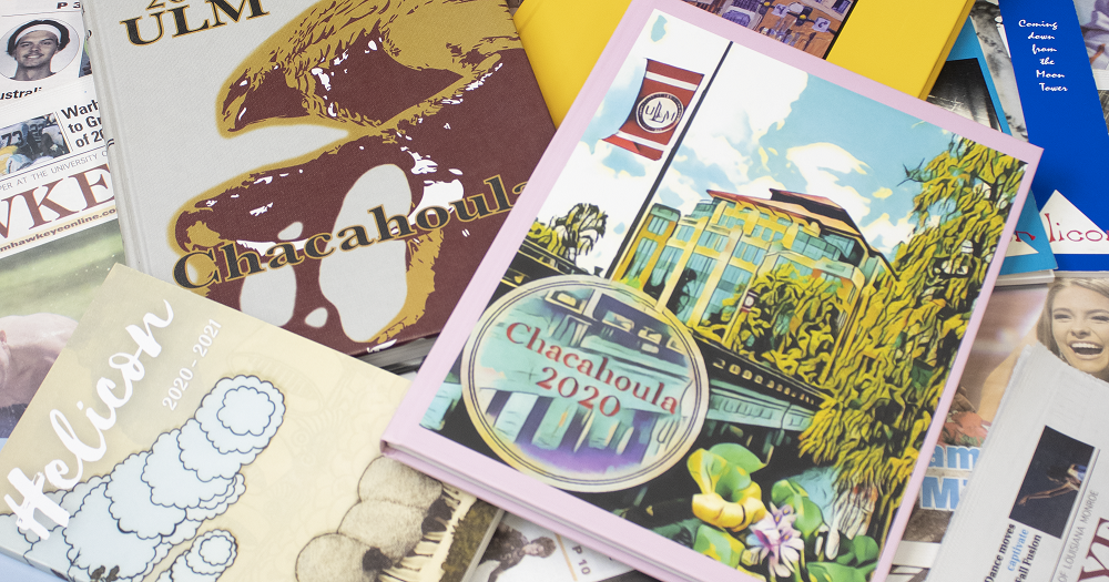 Multiple ULM Chacahoula yearbooks, Helicon journals, and Hawkeye newspapers are spread over a table.