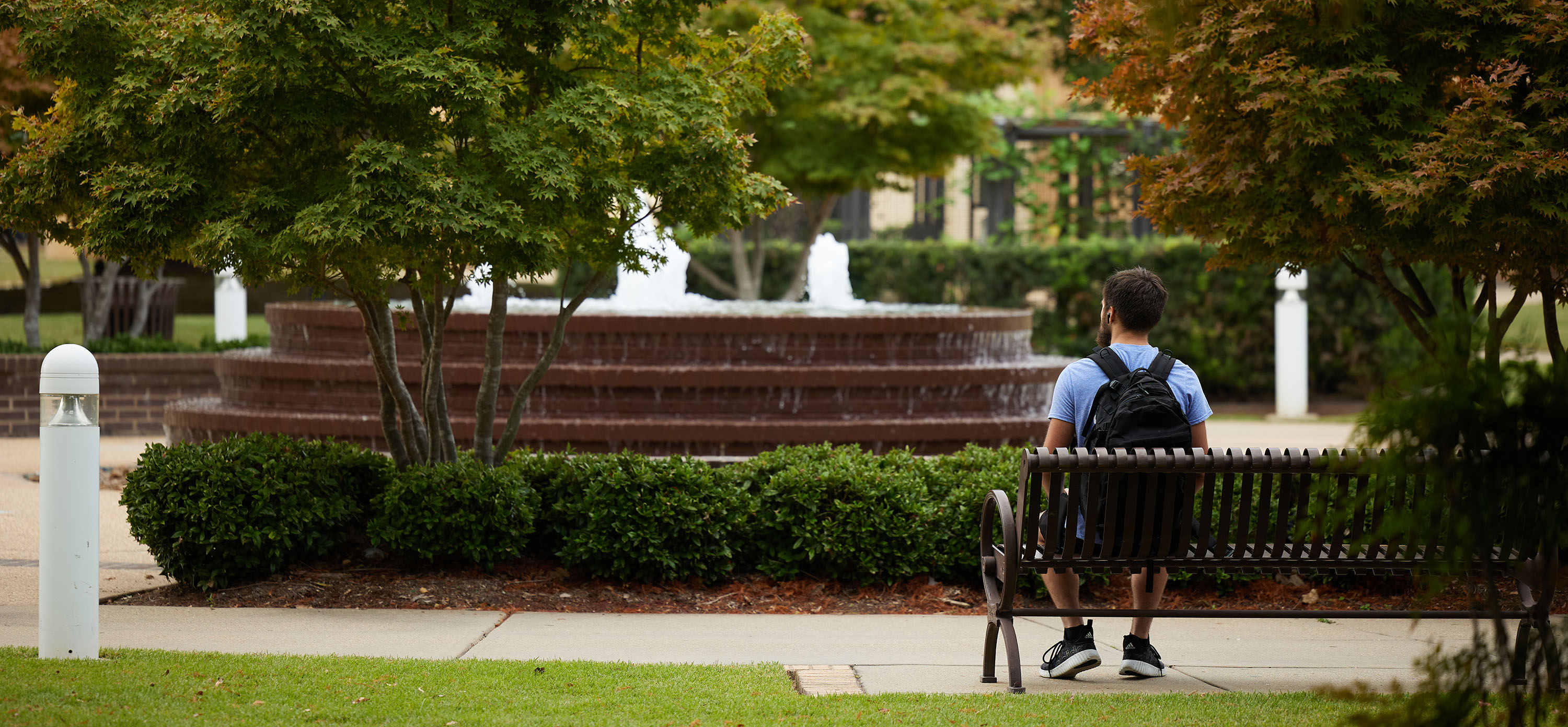 A man sits at a bench in front of a fountain.