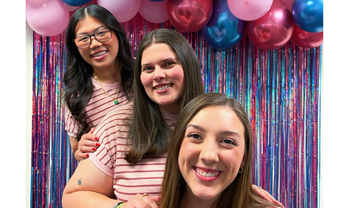 Three KE members in front of balloons and streamers at a KE event.