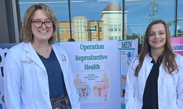 Two College of Pharmacy students standing in front of their presentation board on ULM main campus.