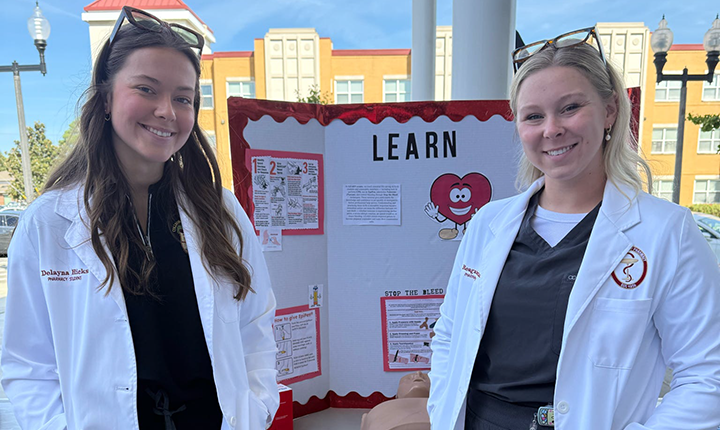 Two College of Pharmacy students in front of presentation board on ULM main campus.