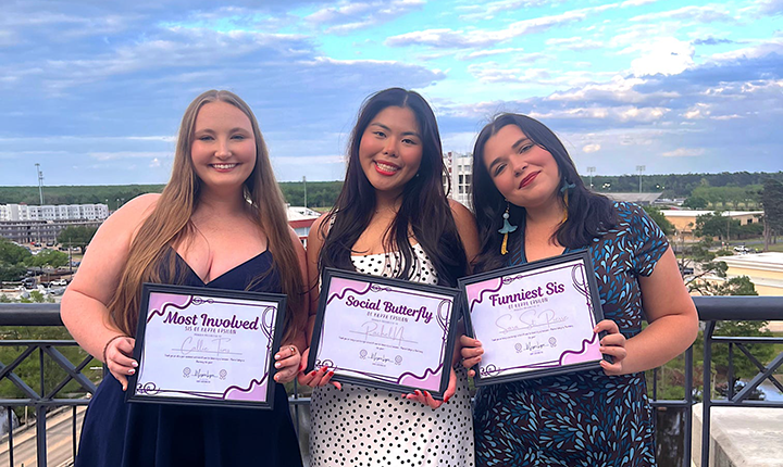 Three KE members holding certificates on the balcony of ULM Library.