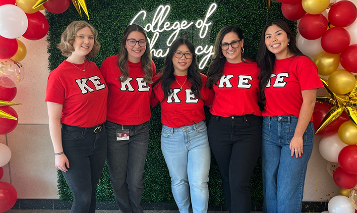 Five KE members standing in front of College of Pharmacy wall.