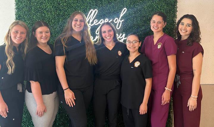 #slide2 ULM Chapter of Christian Pharmacists Fellowship International officers for academic year 2026. Seven female College of Pharmacy students in front of a greenery wall.