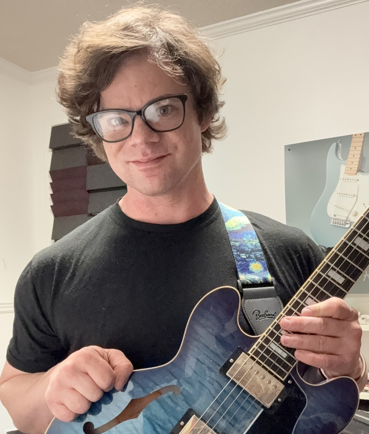 Jae Farmer is holding a guitar and wearing glasses and a black shirt.