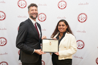 Dr. Joshua Stockley and Aakriti Pant smile at the camera. They hold an award.