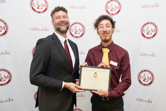 Dr. Joshua Stockley and Beau Benoit smile at the camera. They hold an award.
