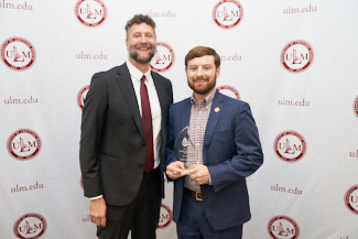 Dr. Joshua Stockley and Ash Aulds smile at the camera. They hold an award.
