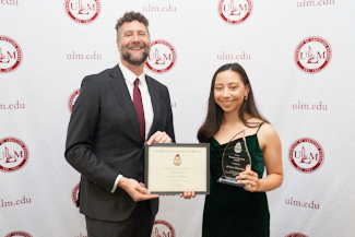 Dr. Joshua Stockley and Ariana Yelverton smile at camera. They hold an award.