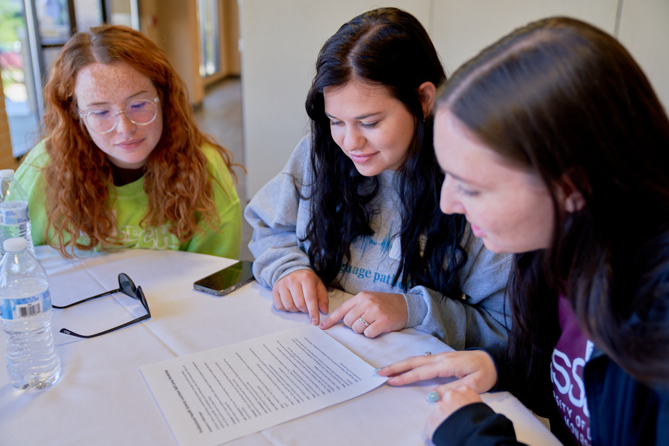 Three students lean in and look at a paper in front of them.