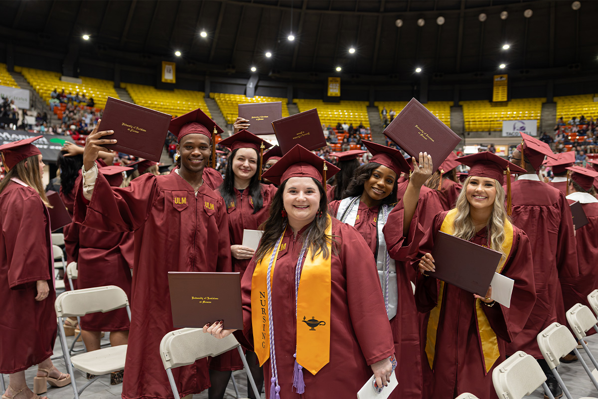 Several ULM graduates in cap and gown hold up their diplomas at the summer and fall 2025 commencement ceremony. 
