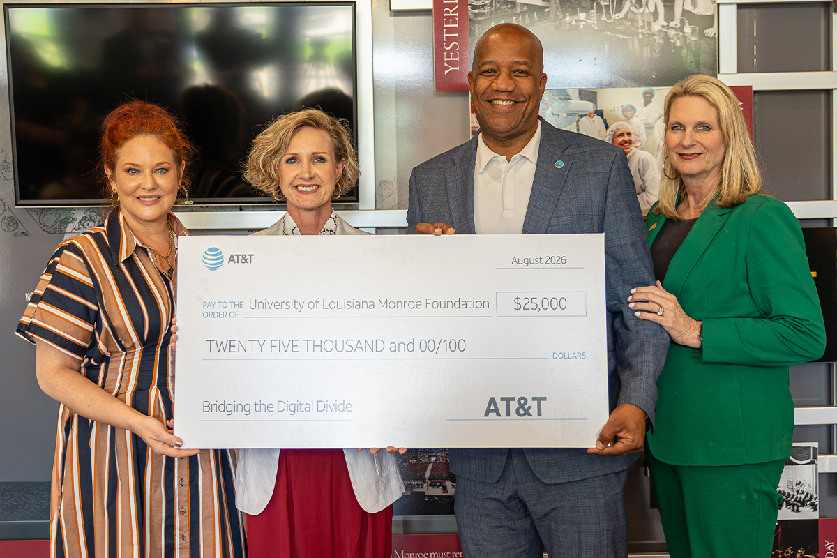 A group of four people hold a large check and smile. 