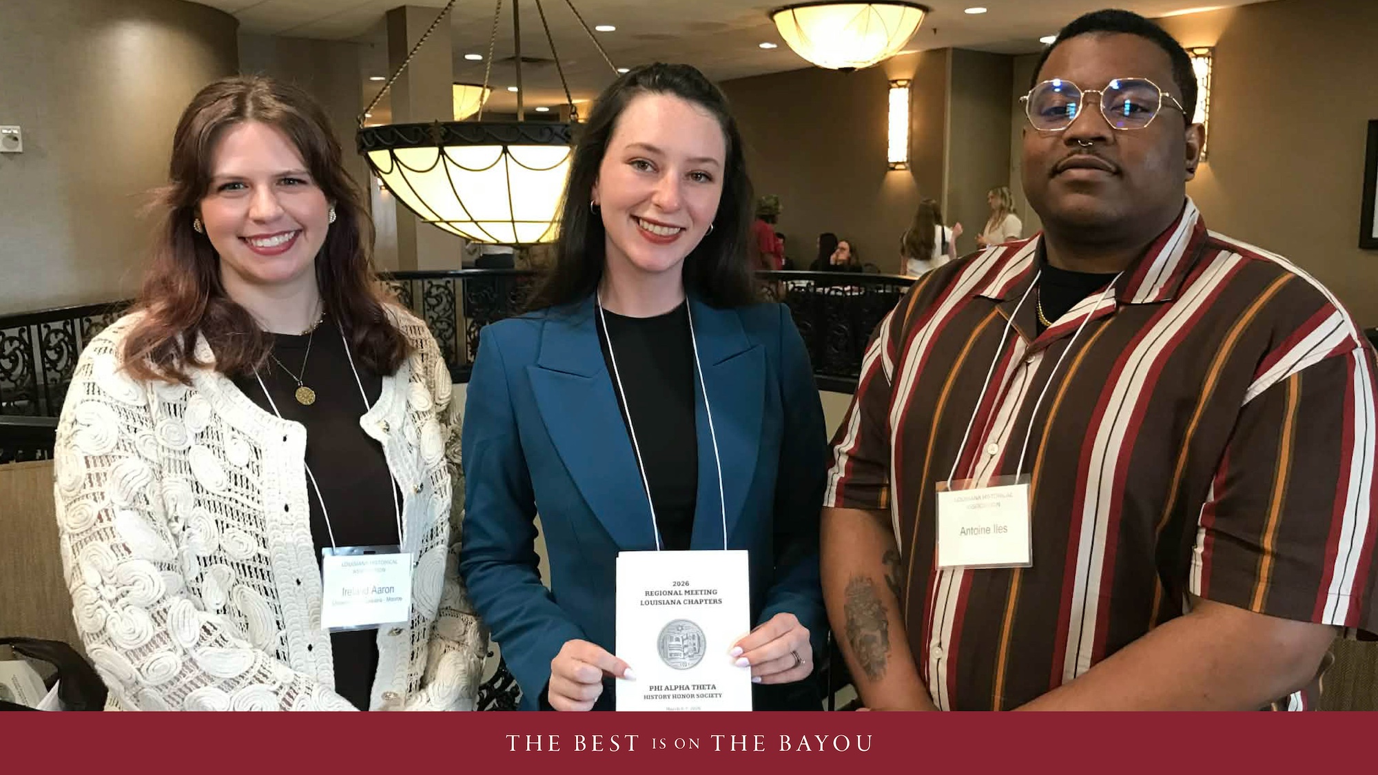 Three people standing in a row smiling. 