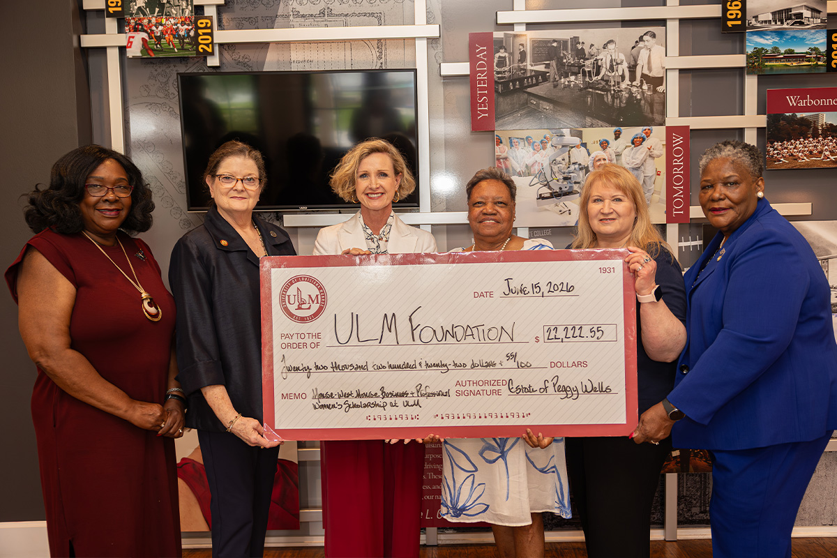 A group of women hold a large check signifying a donation to ULM. 