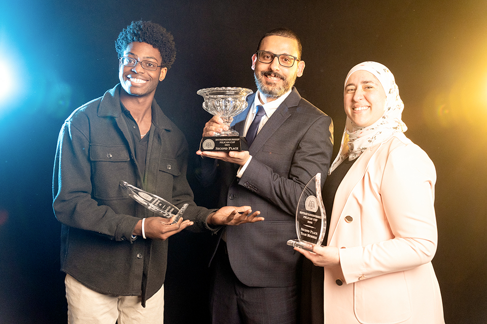 Three people are holding trophies, with one man holding a large trophy and two smaller ones. They are all smiling and posing for a picture.