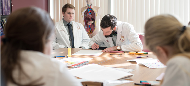 Image of four pharmacy students working on a class project around a table.