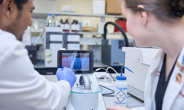 Graduate student explaining the ThermoScientific NanoDrop One to a pharmacy student. Graduate student explaining the ThermoScientific NanoDrop One to a pharmacy student.