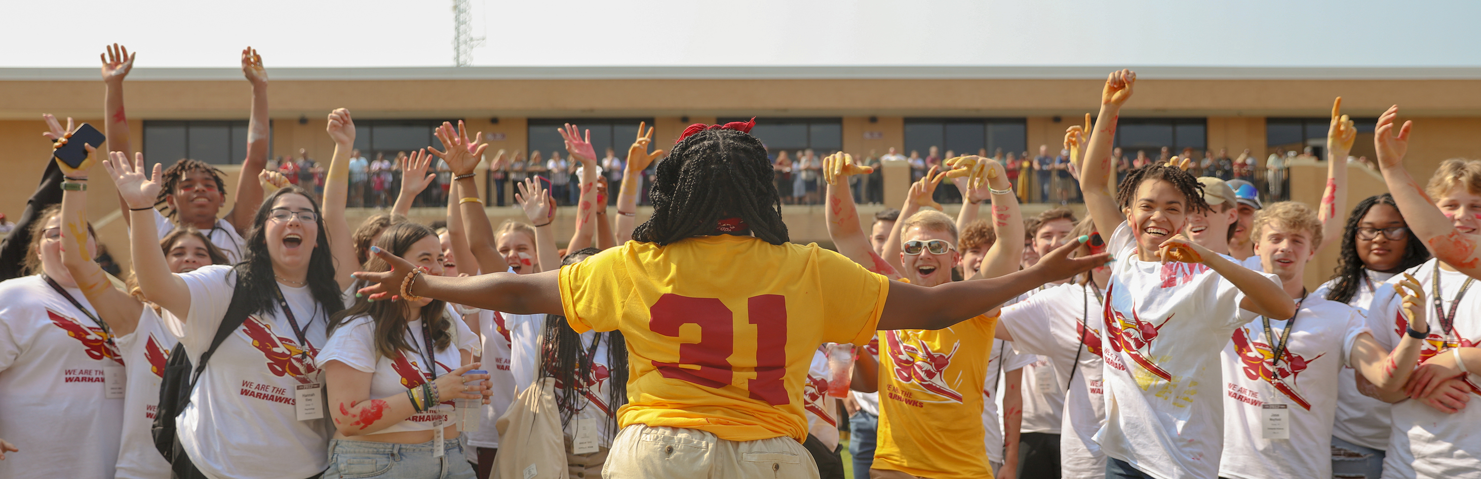 A woman's back is to the camera. She wears a gold jersey with 31 on the back. Her arms are raised and there is a crowd of people cheering facing her.