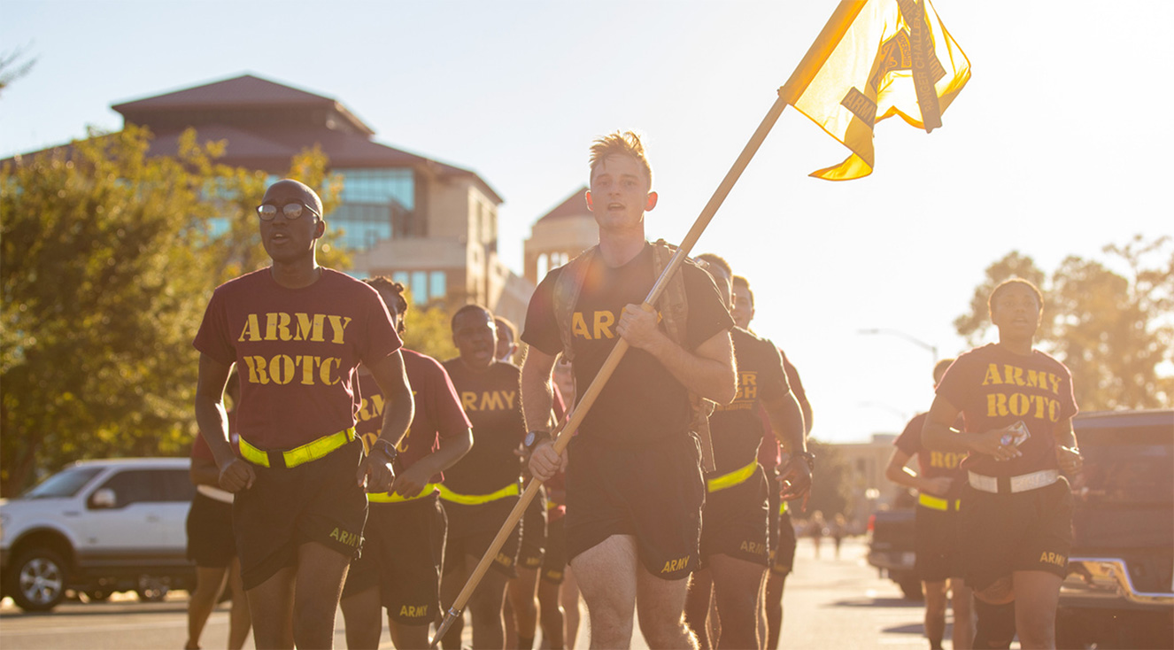 Army ROTC members running with flag through campus