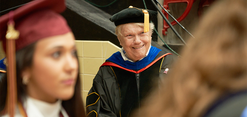 An older person in graduation regalia smiles at younger people in graduation regalia.