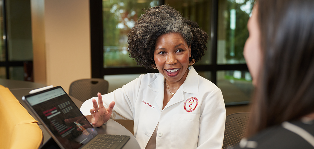 A woman points to a camera and talks to someone whose back is to the camera.