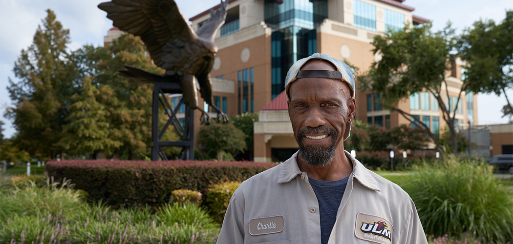 A man smiles at the camera in front of a large, bronze statue of a hawk.